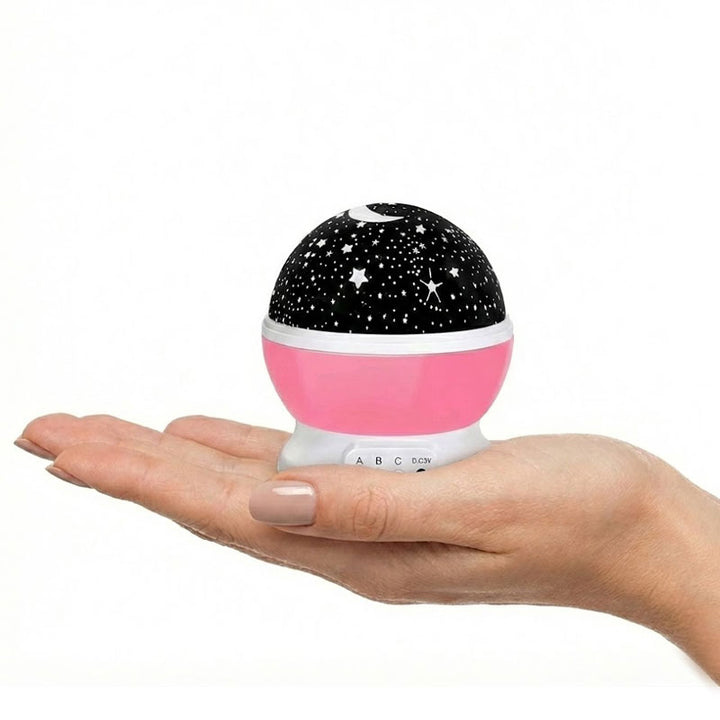 מיני מנורת לילה ומקרן כוכבים לילדים בצבעים ורוד מונח על כף יד
